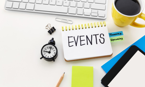 Notebook with events written in it and coffee mug, keyboard, clock around it