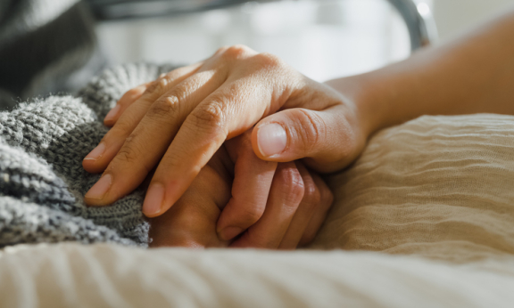 A close-up of a caregiver holding a patient’s hand in comfort.