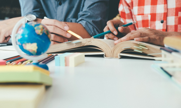 Two people reading a book with a small globe on a table