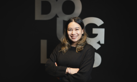 Woman stands smiling with her arms crossed in front of a "Douglas" sign