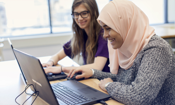 Two students using laptops and smiling