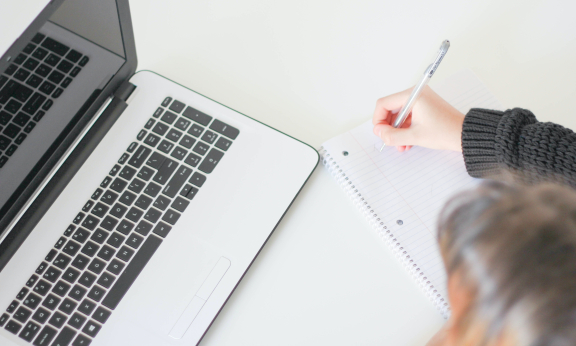 A student writing notes in a notebook from a laptop