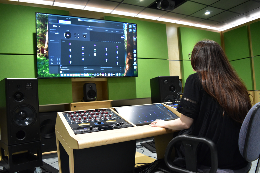 Female student sitting at a sound mixing booth in an audio recording studio.