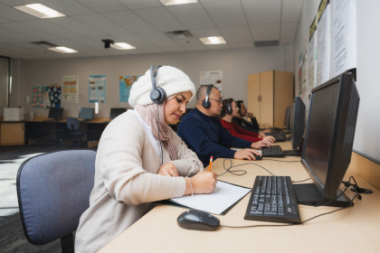 a woman is sitting at a computer writing down into a book