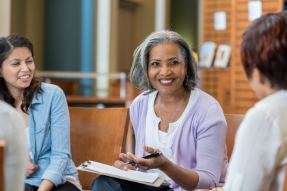 Three people having a discussion. The woman in the center is holding a clipboard and pen.