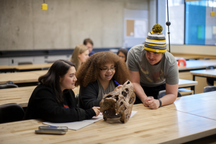 Three students in a classroom looking at an archaeological artifact