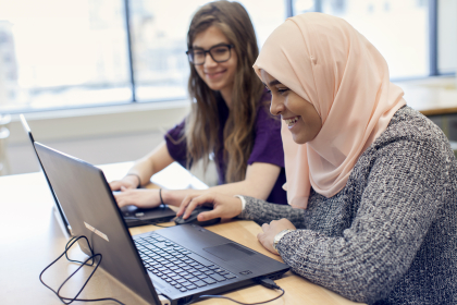 Two students using laptops and smiling