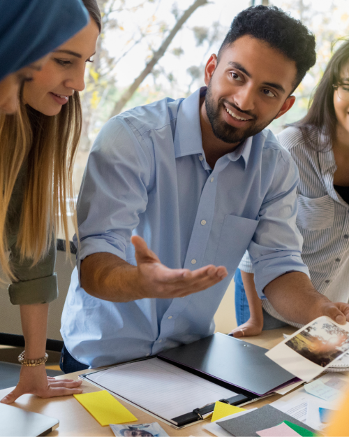 A group of students standing over a table working on a project and smiling