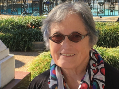 Woman with oval sunglasses smiling in a garden.