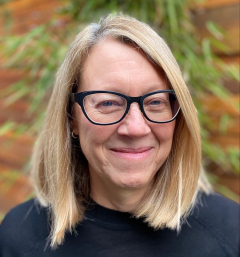 Blond woman with glasses smiling in front of a tree