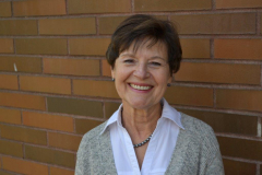 woman in grey shirt smiling in front of a brick wall