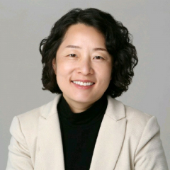 Dark haired woman smiling in front of a grey background