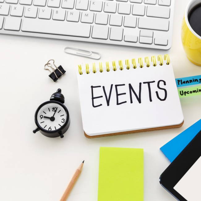 Notebook with events written in it and coffee mug, keyboard, clock around it