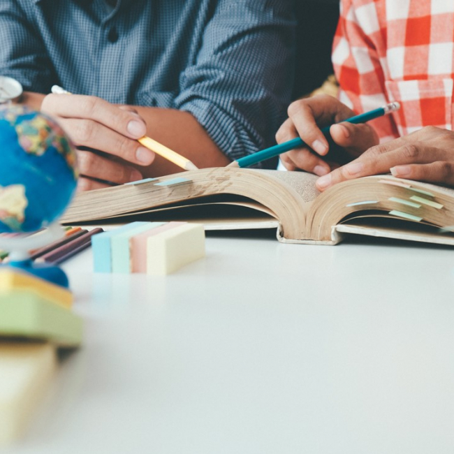 Two people reading a book with a small globe on a table