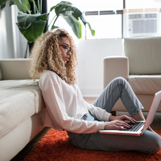 A student sitting next to a sofa and using a laptop