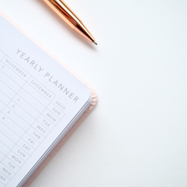 Image of a yearly planner on a white desk with a rose gold pen
