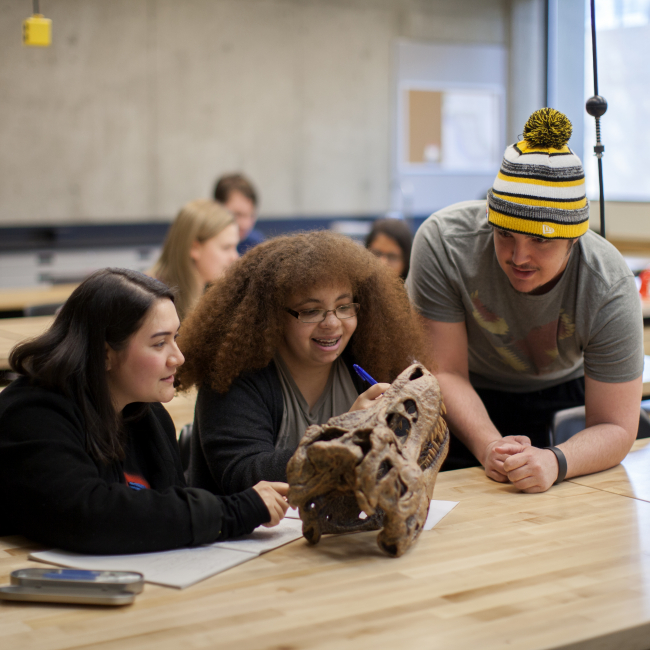 Three students in a classroom looking at an archaeological artifact