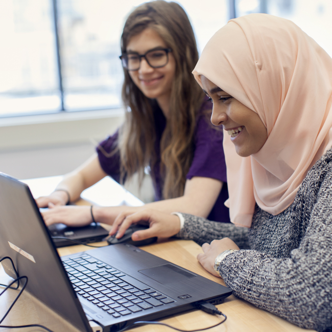Two students using laptops and smiling
