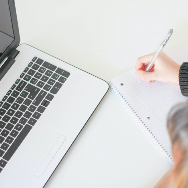 A student writing notes in a notebook from a laptop