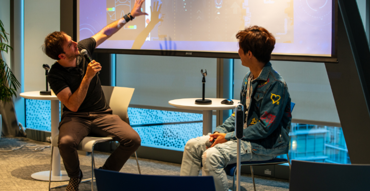 Two video game creators giving a presentation about a game in front of a projector.