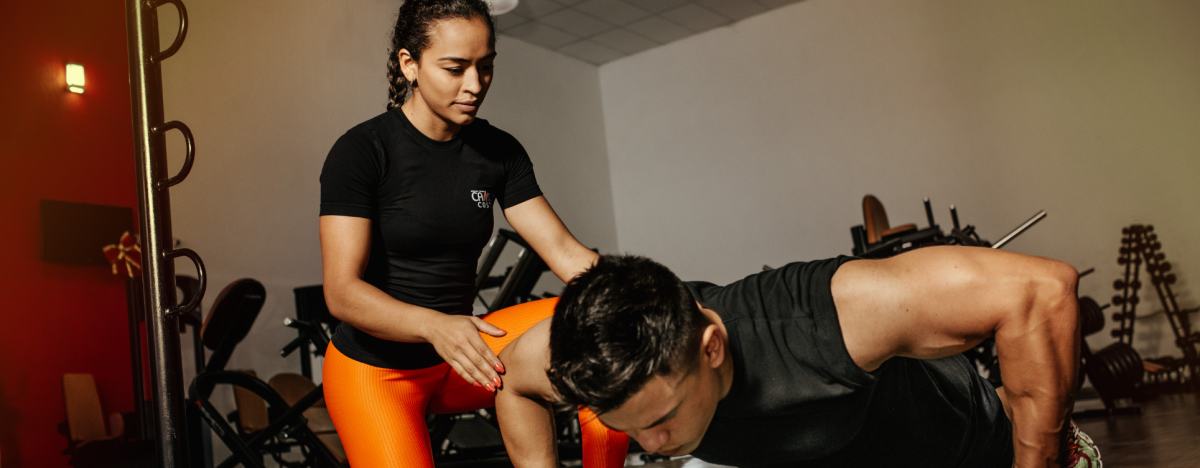 A personal trainer guiding a trainee doing pushups in a gym