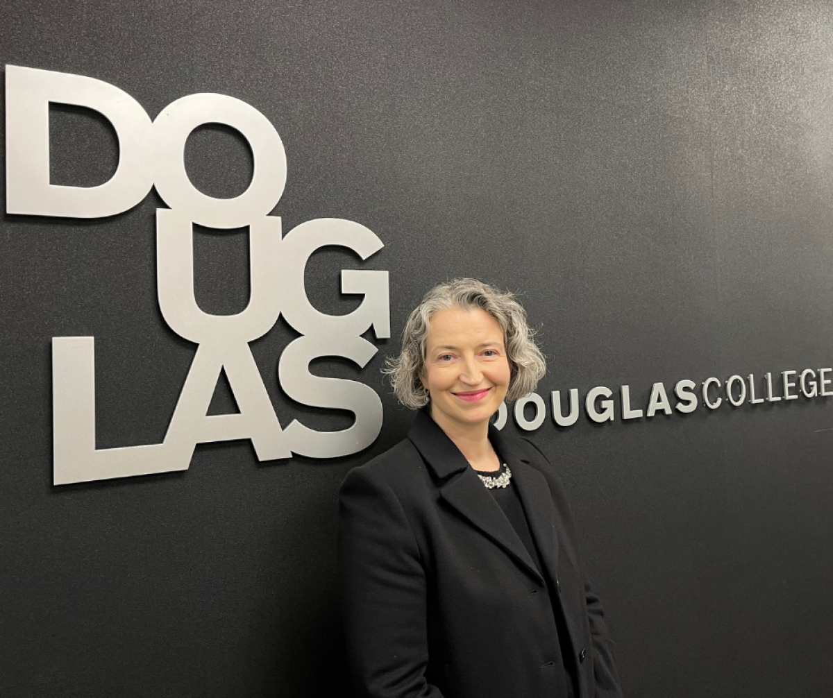 Dr. Manuela Costantino standing in front of a wall with the Douglas College logo on it.