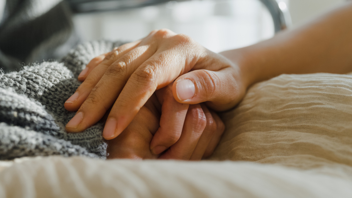 A close-up of a caregiver holding a patient’s hand in comfort.
